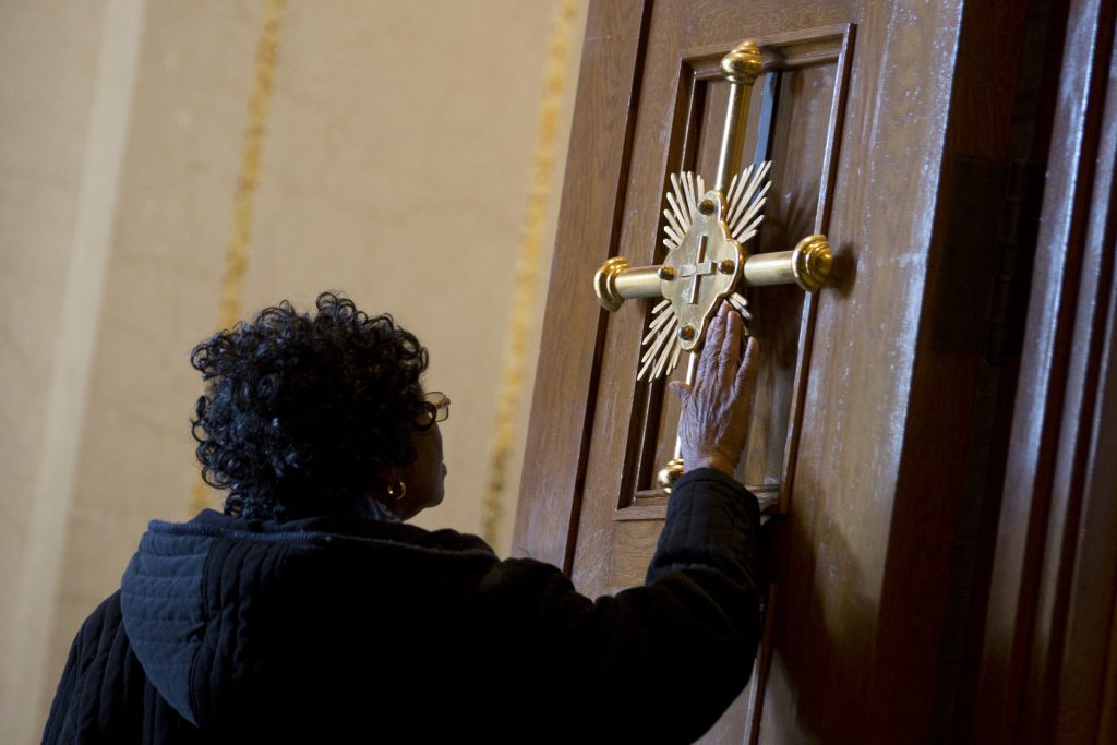 woman touches gold cross on door