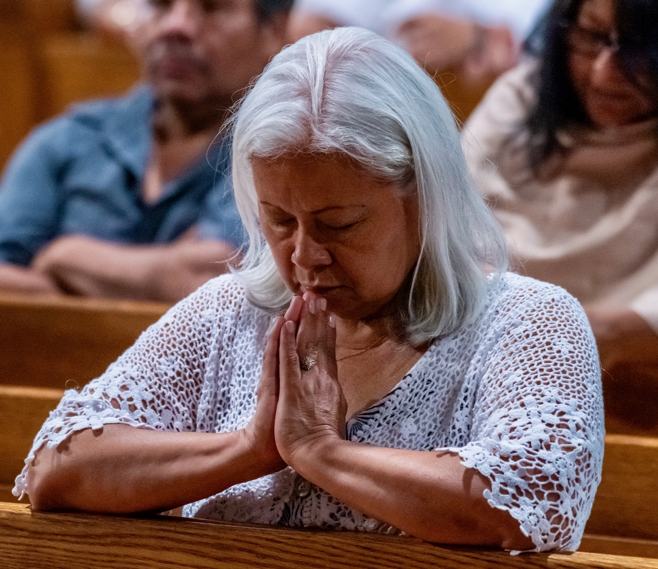 A woman with gray hair prays while kneeling at a pew